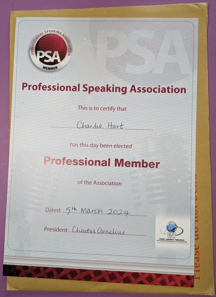 A4 certificate on a C4 manila envelope with Please do not touch in red.
The certificate shows the PSA logo top left, this is PSA in silver writing within a dark red circle with a silver circle border.
In dark red bold text it says Professional Speaking Association, then This is to certify that Charlie Hart has this day been elected Professional Member of the Association.
Dated: 15th March 2024.
President: Chantal Cornelius